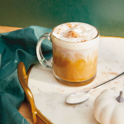 A glass mug full of pumpkin spiced latte, cream on top